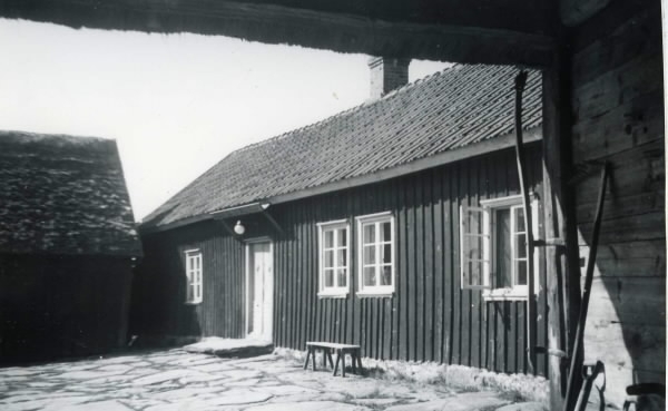 Vy från portlidret in mot bostadshuset och den stenlagda gården på Norrmans bondgård, Värö, Backa nr 7:2. En bänk står vid fasaden nedanför fönstren. (Se även bildnr G8453)