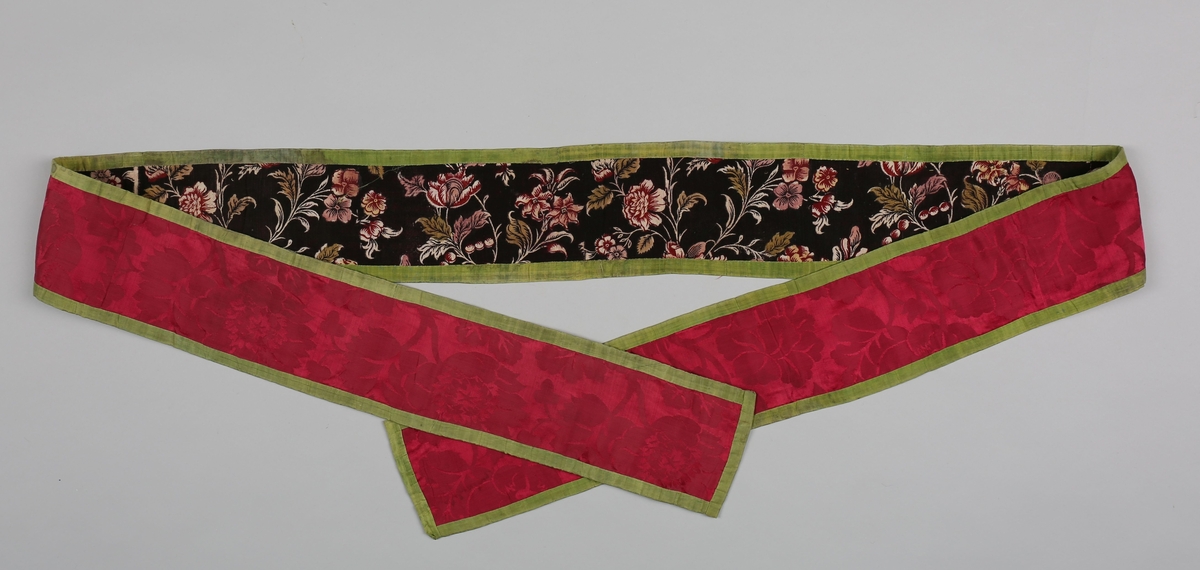 Av rød silkedamask, Skjøtt sammen av fire stykker. Linnen er kantet med grønn silke og fôret med tynt, åpent bomullstøy med påtrykt blomstermønster og sort bunn.