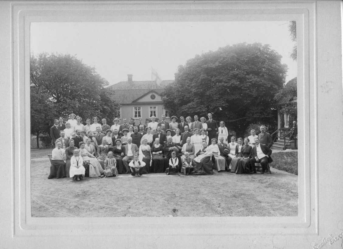 En gruppbild med ett stort antal kvinnor, män och barn på en gårdsplan.