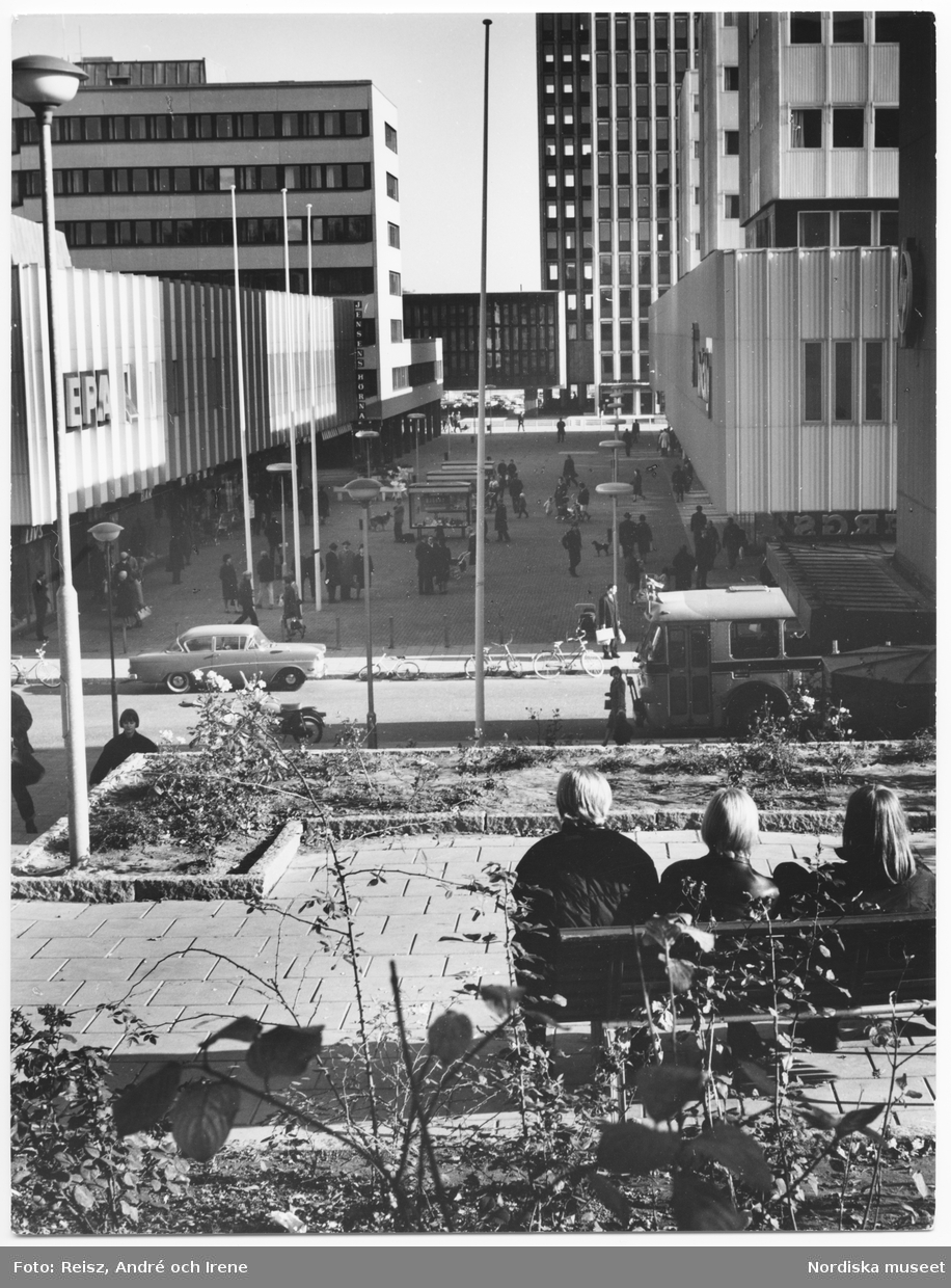 Stockholm. Utsikt över Solna centrum, EPA, människor i rörelse på gågatan . I förgrunden en parkbänk med tre ungdomar.