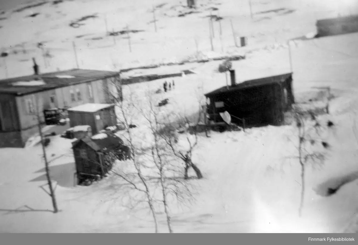 Gruvebyen Bjørnevatn. Brakka til venstre var butikken til Johansen. Øverst til høyre i bildet er det første posthuset, etter krigen. Midt på bildet er det en bolig. Det er vinter og snøen ligger på bakken