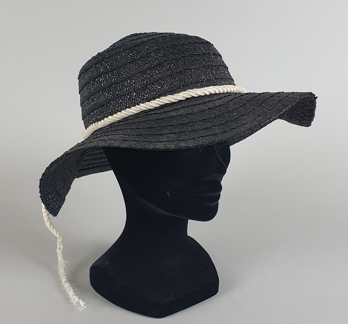 Mørkeblå (svart) hatt av plast, med hvitt plastbånd rundt pullen.