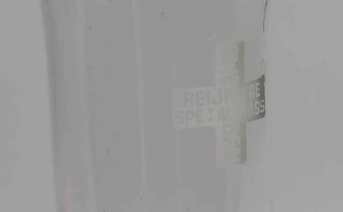 Cylinderformat glasrör för kemiskt bruk.
Rakt rör som är vidgat i den ena änden. På sidan ett graverat likarmat kors med texten "REIJMYRE SPECIALGLASS SWEDEN".