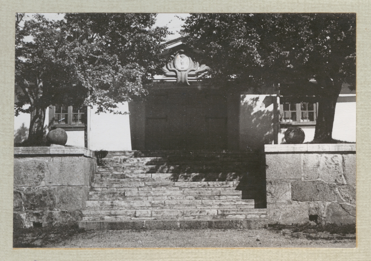 Bilden visar Chapmansporten på Karlskronavarvet samt tillhörande trapp och två träd som flankerar porten.