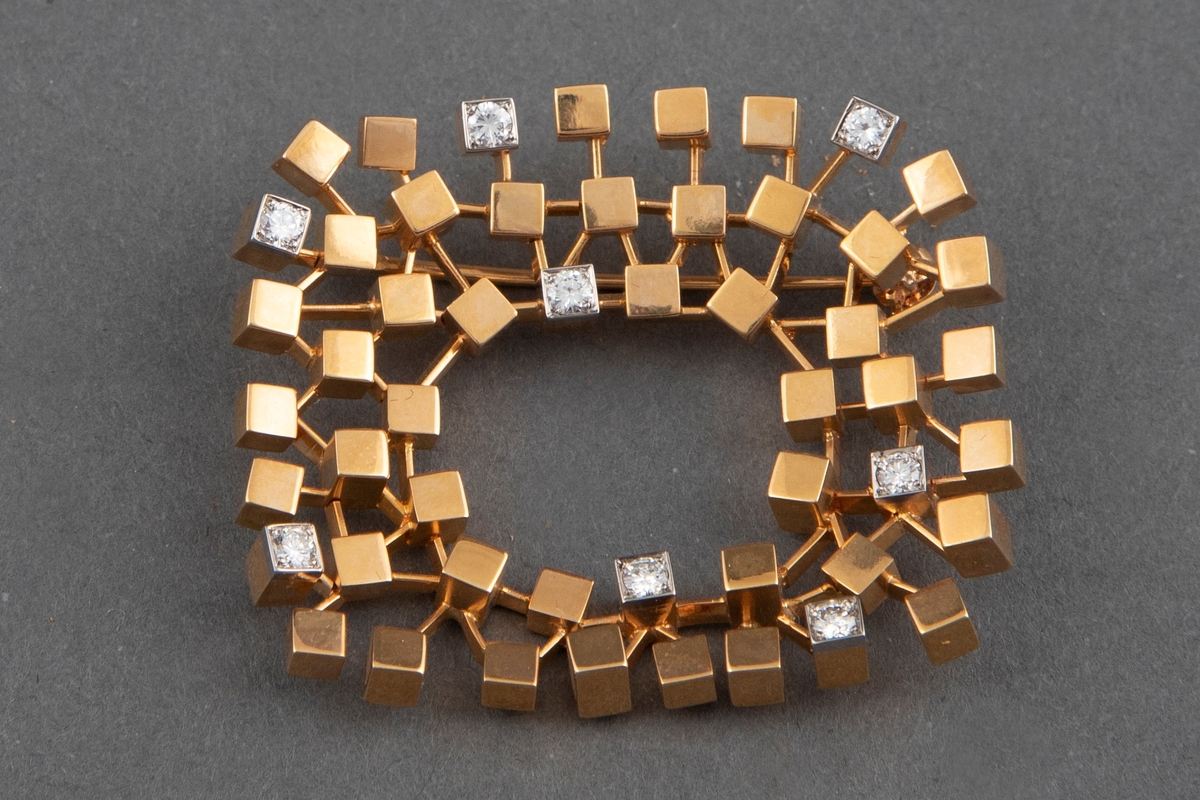 Brosje bygget opp av små kubiske elementer av vekslende lengde med endeflater som er cirka 3 x 3 mm. Brosjen er laget av 18 karat polert gull med 8 briljanter. Den er åpen i midten og har en nål på baksiden.