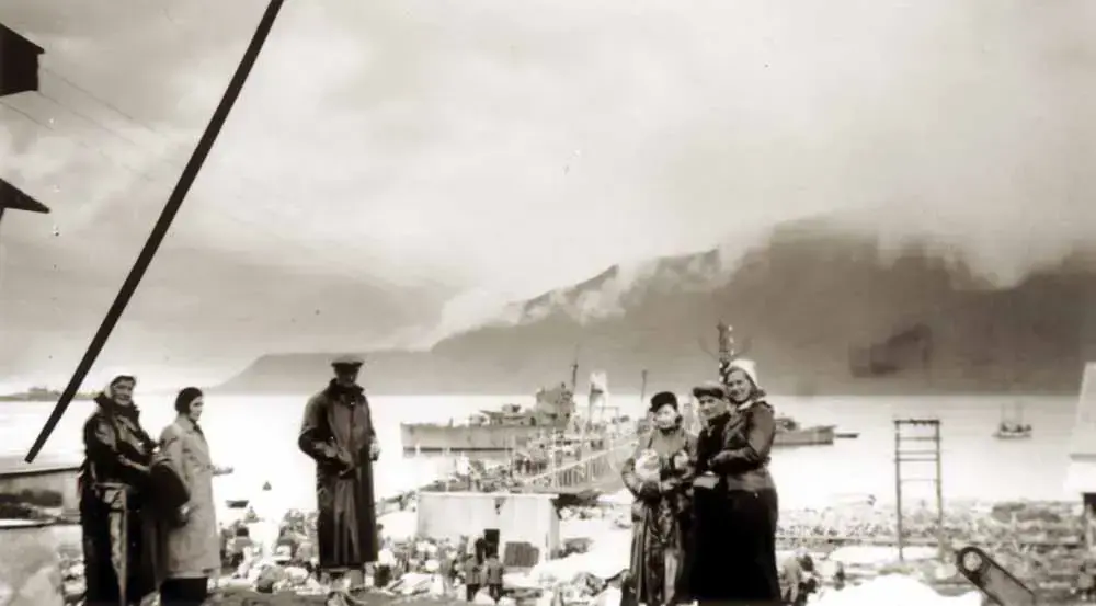 Mennesker evakueres fra kaia. Marinefartøy, fjord og fjell i bakgrunnen.