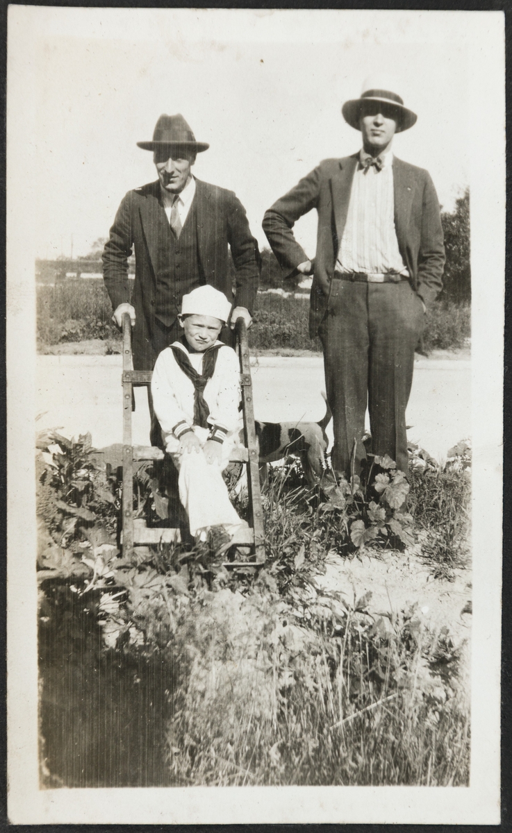 Bjarne Fixdal t.v. og en mann i en hage i Ouster ave. Billy sitter i matrosdress på en liten stige. En hund står bak dem.