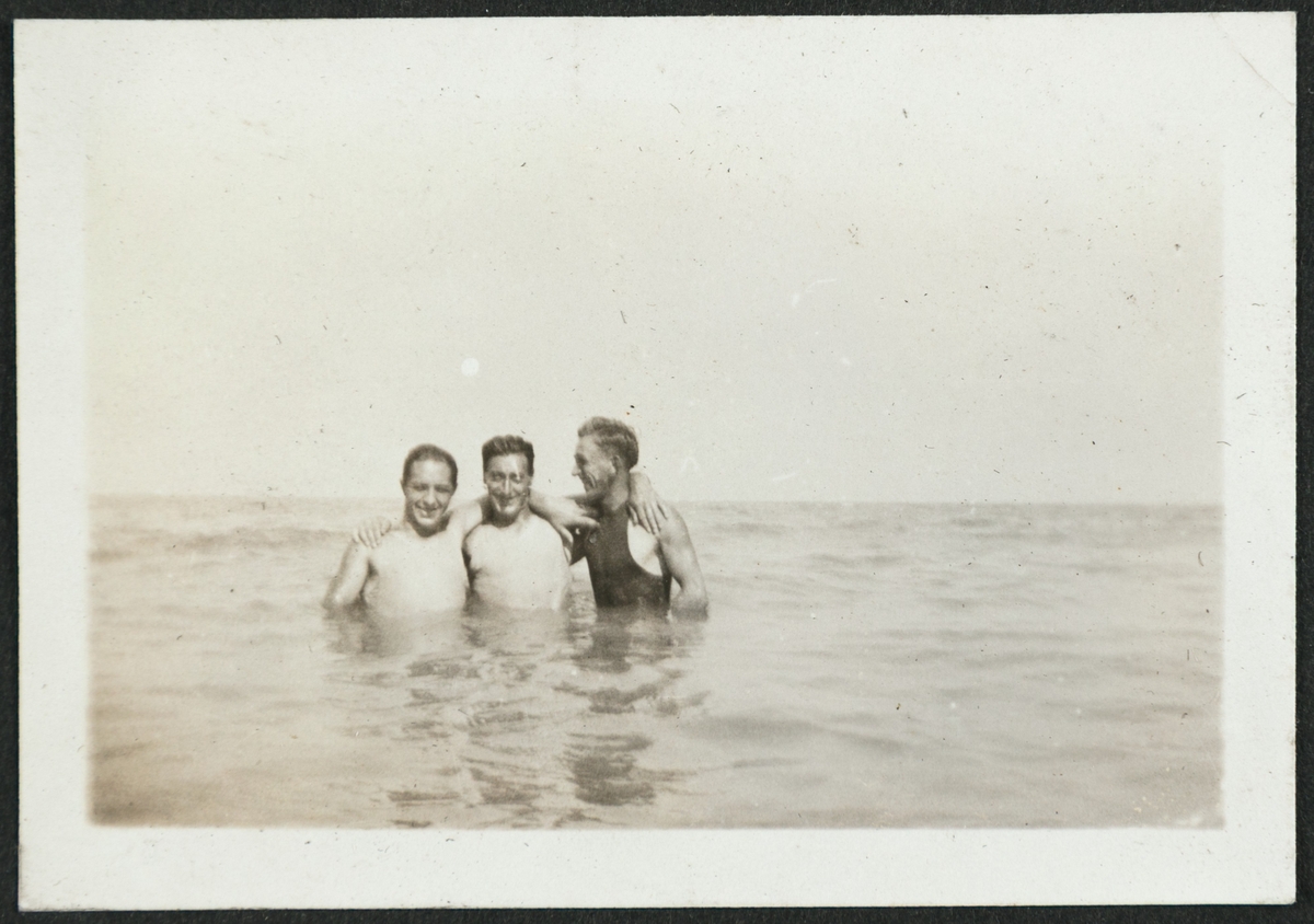 Tre badende menn poserer med armene rundt skuldrene til hverandre stående med vann til livet.