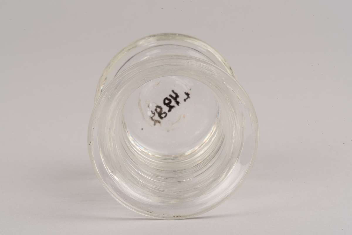 Runt glas med insvängd midja, dekorerad med fyra lodräta vulster runt glasets mitt.
Glastypen kallas länsmansglas eller fyrbandsglas.