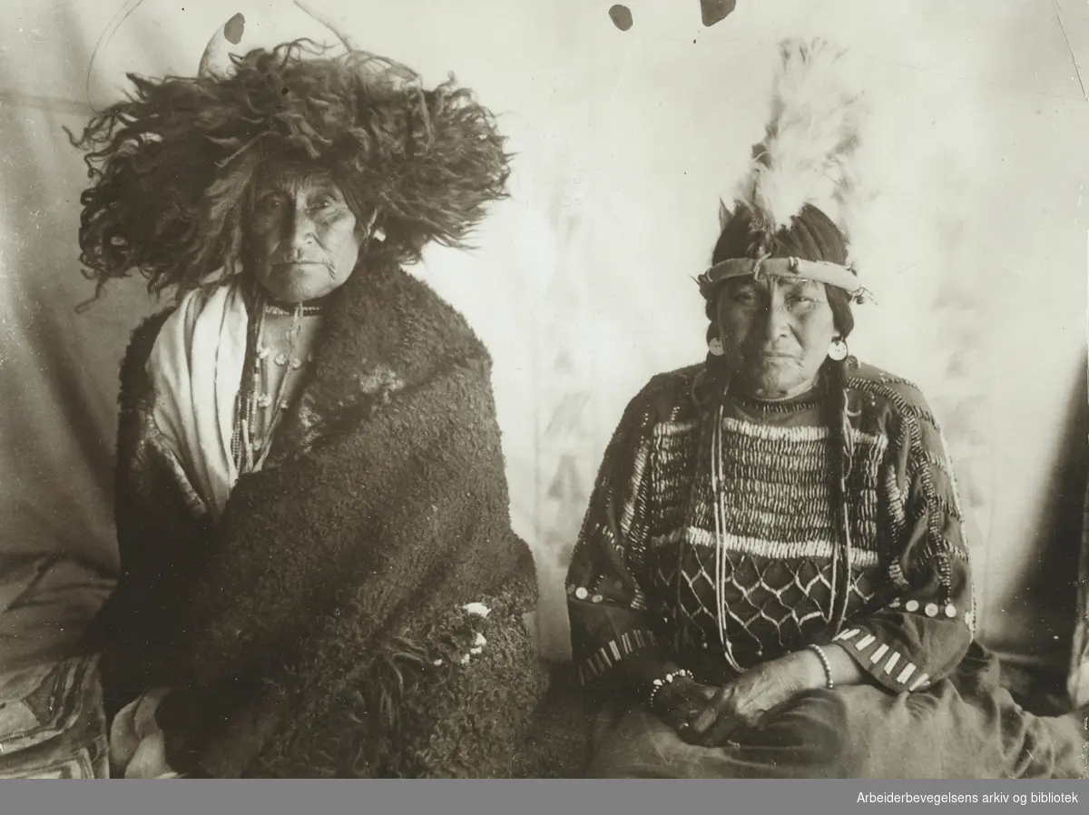 Billedreportasje fra et reservat for amerikanske urfolk. "To indianerkvinner bærer magiske hodeplagg. Denne hodebekledning har i århundreder har blitt betraktet for å ha magisk inflytelse". Udatert. Uten stedsangivelse. Arbeidermagasinet.