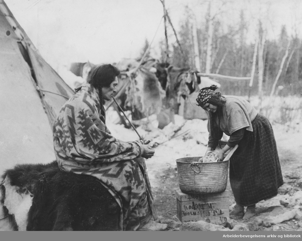Billedreportasje fra et reservat med amerikanske urfolk. "Indianerhusbonden tar sig en røik mens kona sliter med klæsvasken". Udatert. Uten stedsangivelse. Arbeidermagasinet.