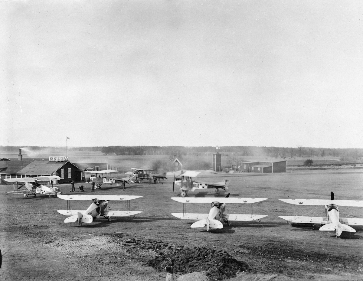 Flygkompaniets verkstadsområde på Malmen. Tre flygplan FVM Tummeliten märkta "Hjärter ess", "Klöver ess" samt "Ruter ess". I bakgrunden flygplan Albatros och Phönix Dront.