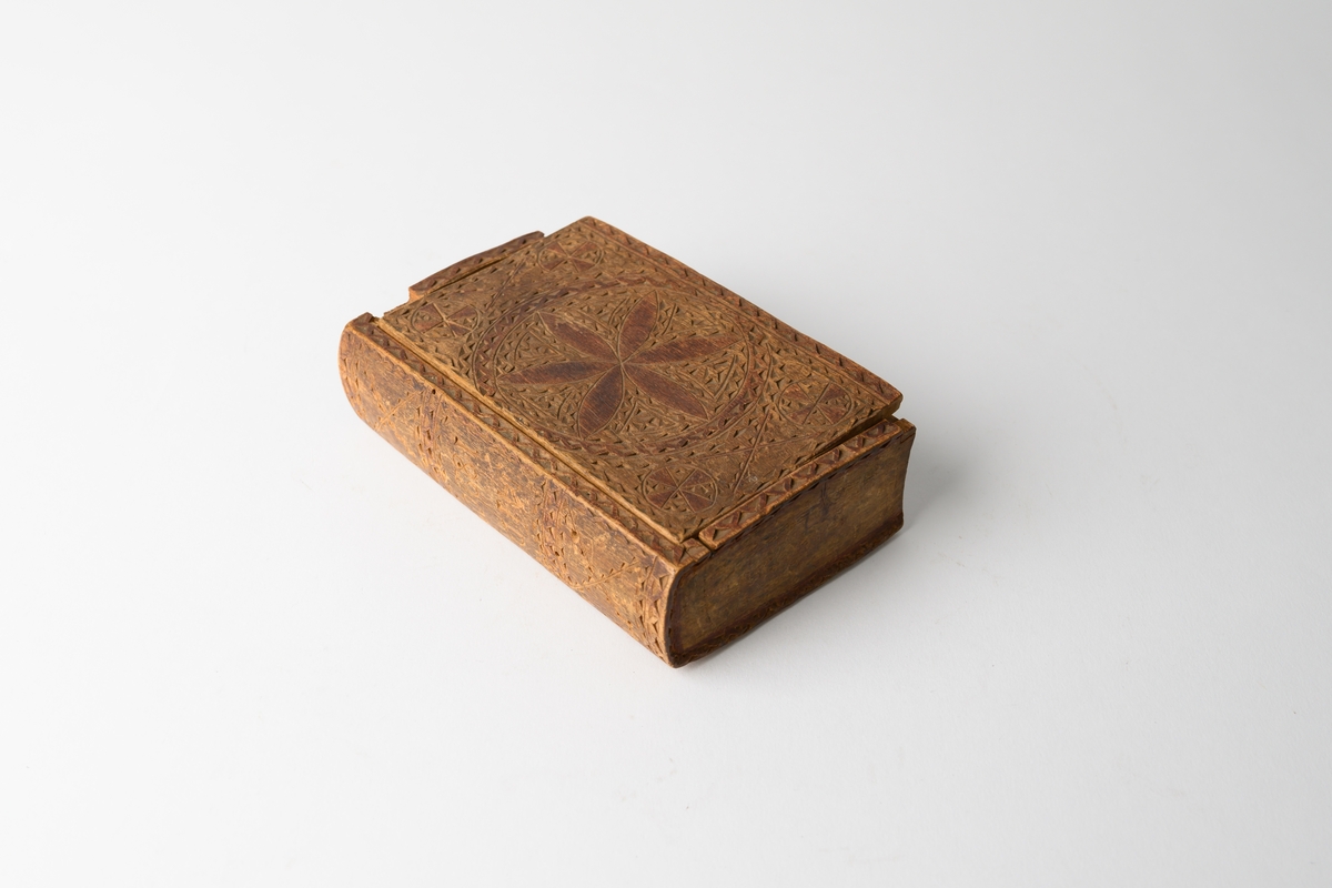 Skrin (ask) av trä i form av en bok. Rikt dekorerad i karvsnitt, med spår av röd färg. På ryggen snidade initialer och årtal: "MSD", "1820".