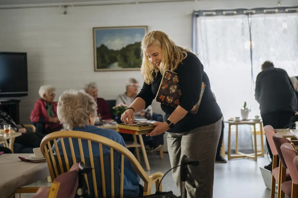 En smilende dame snakket med en eldre person som sitter i en stol