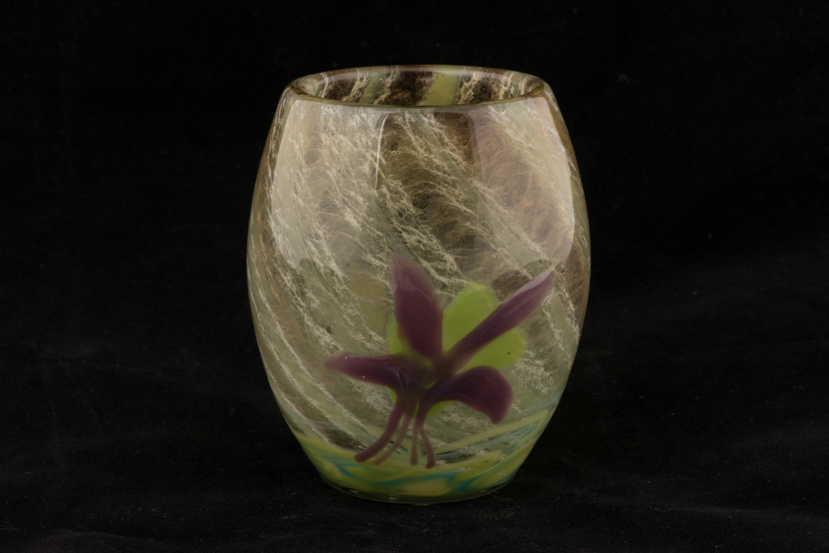 Välsad glasvas i jugendstil.
Svagt bukig vas med växtmotiv. Invälsad spiralvriden flockig glasmassa i vitt, gröngult, grönblått och mörkblått. Påklippt och invälsad blomma i form av en violett akleja samt ett grönt blad.