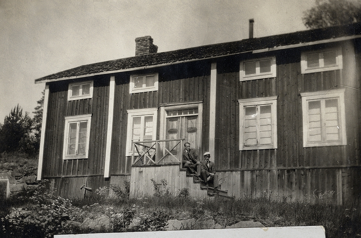 En mangårdsbyggnad med förstukvist och trappa, där det sitter två unga män, den ena med studentmössa (möjl. Edvin och Gustaf Åström).