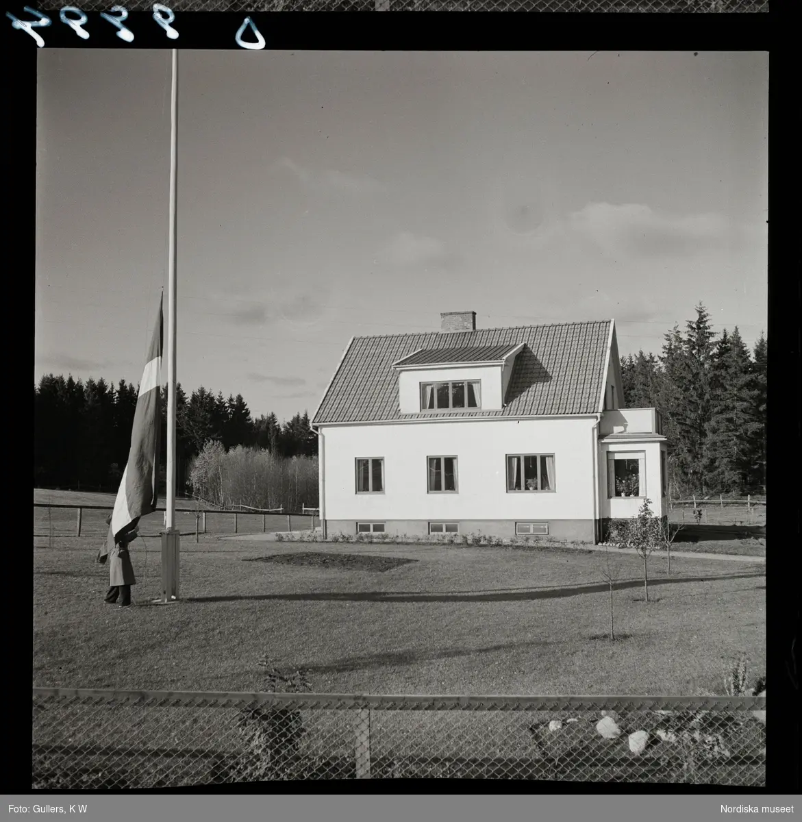 564 Vårgårda Havregryn. En man hissar svenska flaggan framför ett hus.