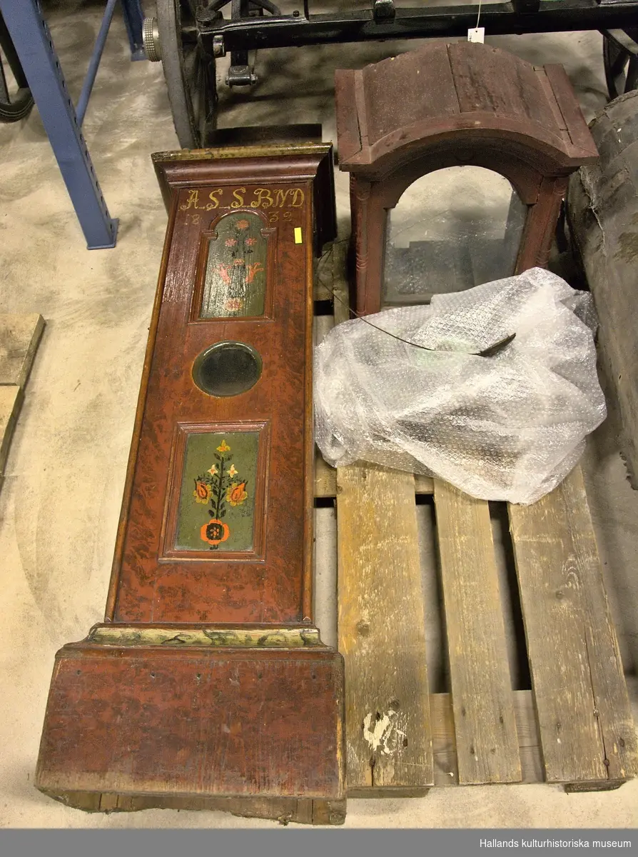 Golvur. Urtavlan av tenn med romerska siffror. 4 stycken triangelformade hörndekorationer av tenn. Över urtavlan en rund tennplatta med inskriften: 1794, B A S.
Träfodral av rak modell. Livets hela framsida upptages av en högerhängd dörr med ett runt, glasat hål på mitten samt två stycken spegelfält. Dörren stänges med en trävarvel. Målad röd-brun, fot och huvud med grön list. Spegelfälten har grönblå botten och vardera har en blombukett av röda och vita blommor. Överst på dörren är med vit färg målat: A S S B N D, samt årtalet 1832.