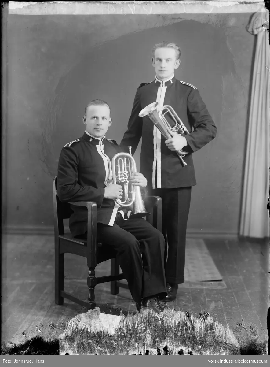 To musikanter fra Frelsesarmeen med instrumenter. Begge kledd i uniform med bokstaven F på jakkekragen. Instrumentene er blåseinstrumenter, en mellofon til venstre og sannsynligvis ett flygelhorn til høyre.