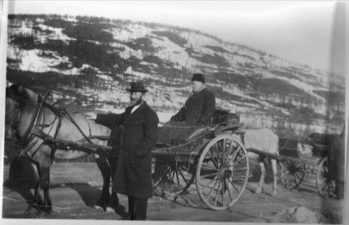 Hest og vogn, en mann står ved hesten og en mann sitter i vognen.