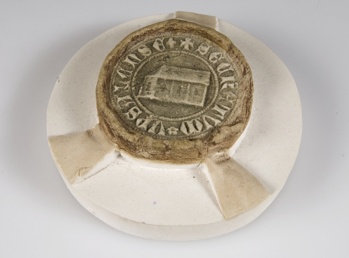 Gipsavtryck av brunfärgad gips på rund gipsplatta av Uppsala stads sigill (sekret) 1410 3/11 1358. Kyrkobyggnad och text "SECRETUM UPSALENSE".