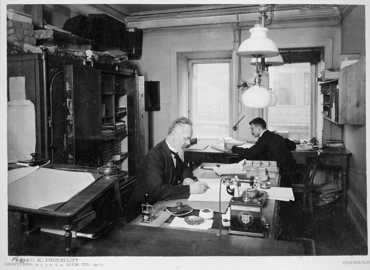 Postdirektonens i Stockholms distrikt kassaexpedition i posthuset vid Rödbodtorget 1903.

Från vänster: Hj. Syk, P Vretblad.