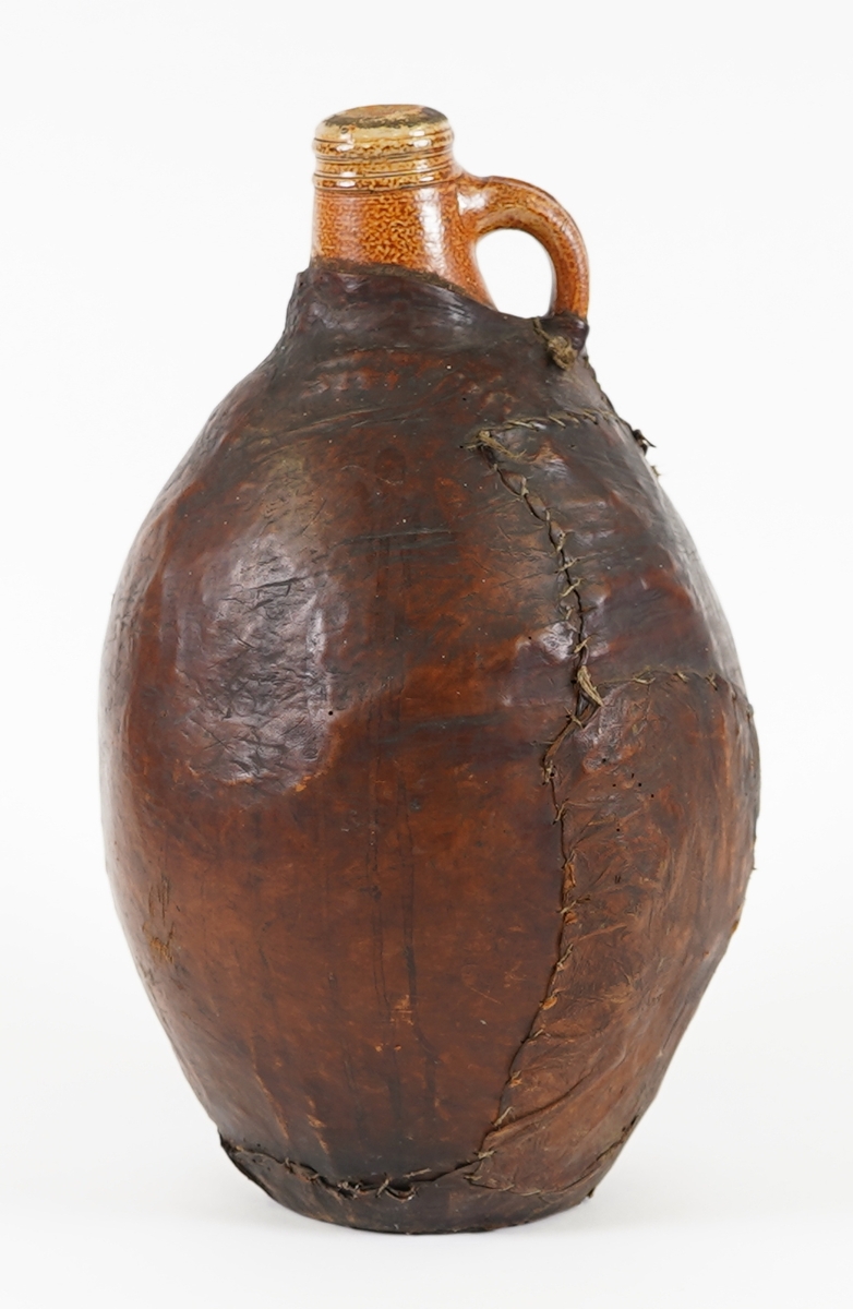 Vinkukke i keramikk, trukken med lær. Ovalt forma korpus, med smal hals. Hank på halsen.