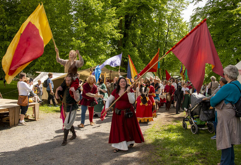 Opptog av mennesker kledd i middelalderkostymer og med fargerike flagg.