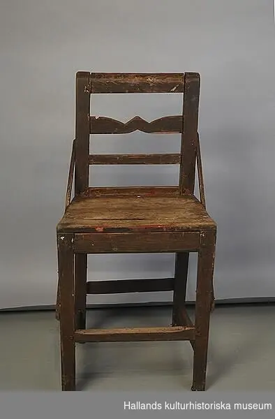 Stol i brunmålat trä. Två trälister går på var sin sida om stolen diagonalt från ryggstödet ner till de främre stolsbenen.