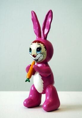 Kanin i plast. Kaninen er rosa og hvit. Den smiler og i hånda har den en gulrot.