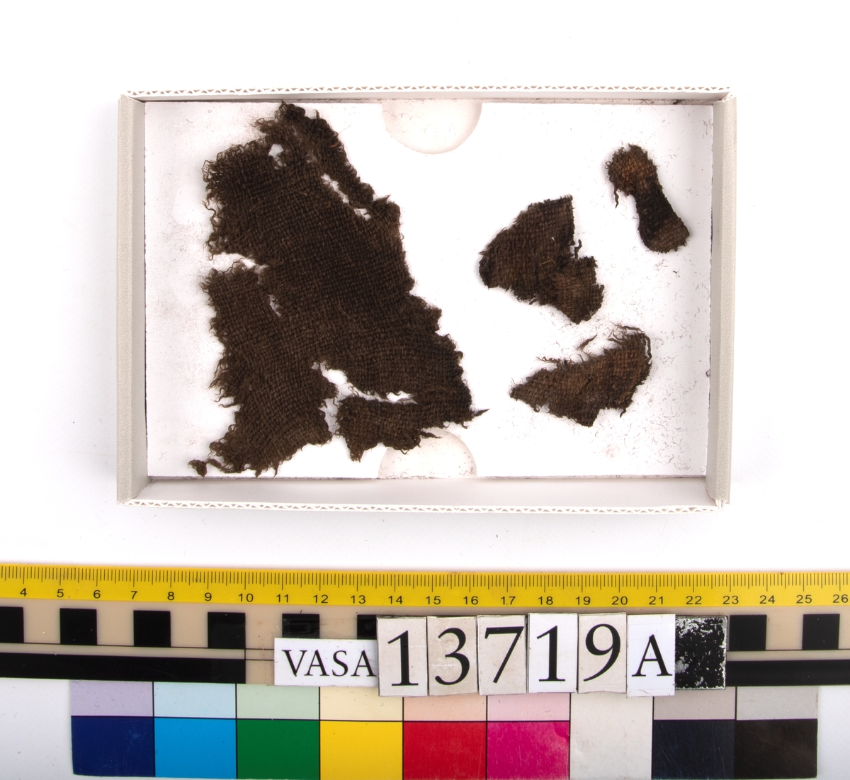 Textil.
33 textilfragment uppdelade på fyndnummer 13719a-c.
Fnr 13719a består av 5 fragment av ull vävda i tuskaft.
Fnr 13719b består av 14 fragment av ull vävda i tuskaft. Tyget har troligen varit valkat på ena sidan.
Fnr 13719c består av 14 fragment av ull vävda i tuskaft. Tyget har troligen varit valkat på ena sidan. De tre största fragmenten är kilformade. Fragmenten har flera originalkanter med spår av sömmar.