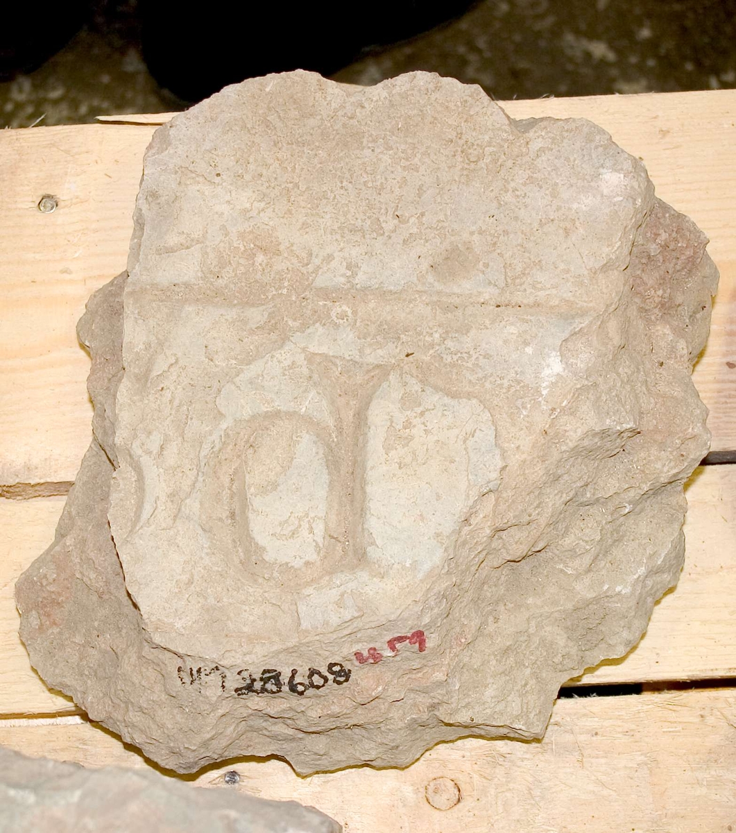 Fragment av gravhäll av kalksten, flagnande brottytor, med inhuggen bokstavsbård, bokstaven P.