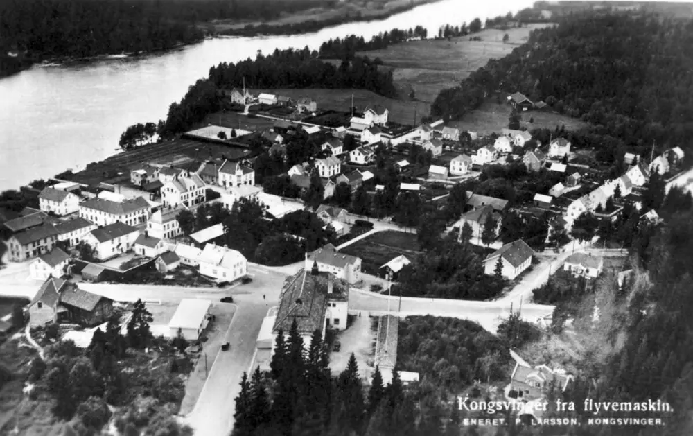 Et svart-hvitt postkortet fra ca. 1930. Kortet viser Midtbyen i Kongsvinger fra lufta. Glomma øverst til venstre i fotoet.