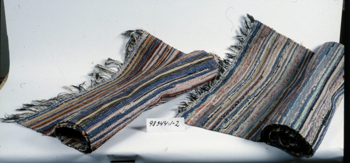 Handvävda trasmattor av både ylle- och bomullstrasor i ett flertal färger.
Varp av bomull.
Knuten frans i kortändarna i svart och vitt.

Neg.nr. 1987-04