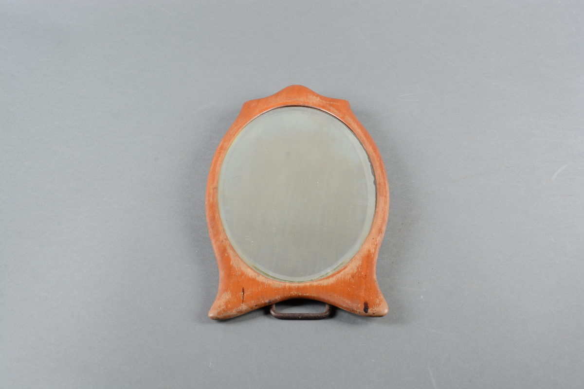 Ovalt speil med treramme. Rammen følger speilets form med tre avrundede spisser på toppen og to avrundede føtter nederst. På baksiden er det festet et stativ av metall.