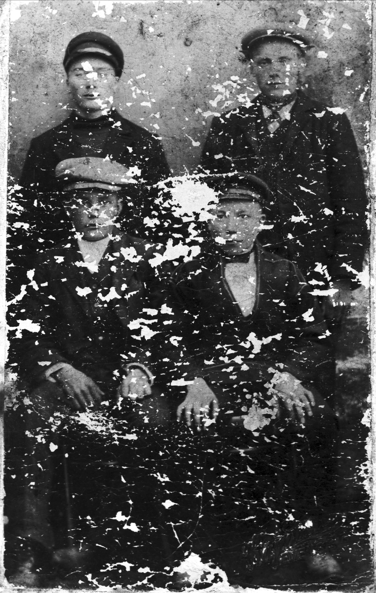 Studioportrett av fire menn, to sitter og to står bak. Bildet er skadet.