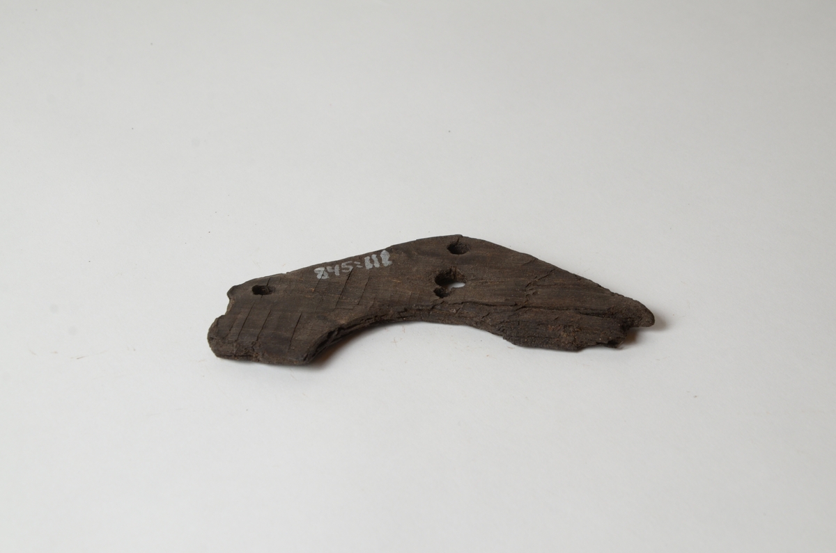 Skiva av trä, sju mm tjock med hål. Fragment av överdelen till en råhudslykta.