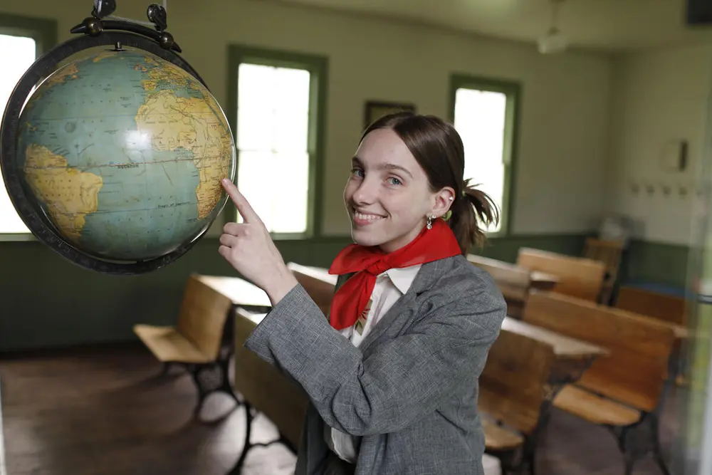 Sommerguide Rebekka i skolehuset. Skolehuset er en av de åtte antikvariske bygningene på museet. På bildet ser du Rebekka som peker på en globus.