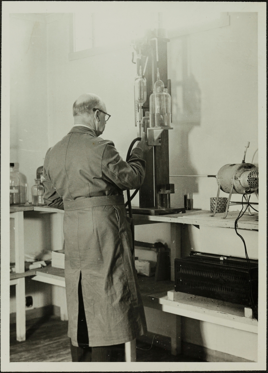 Ein mann i frakk står attmed eit apparat i laboratoriet på Sandnes Auducerverk.