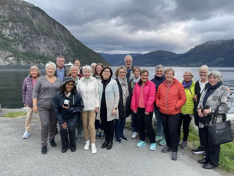 19 medlemmer av Kraftmuseets vennelag på høsttur til Ytre Arna, bilete er tatt med fjord og fjell i bakgrunnen av gruppen. Foto.