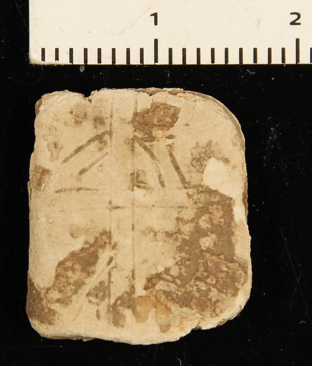 Sammenfoldet plate av blylegering av type runeamulett med innrisset korsformet figur på den ene siden. 