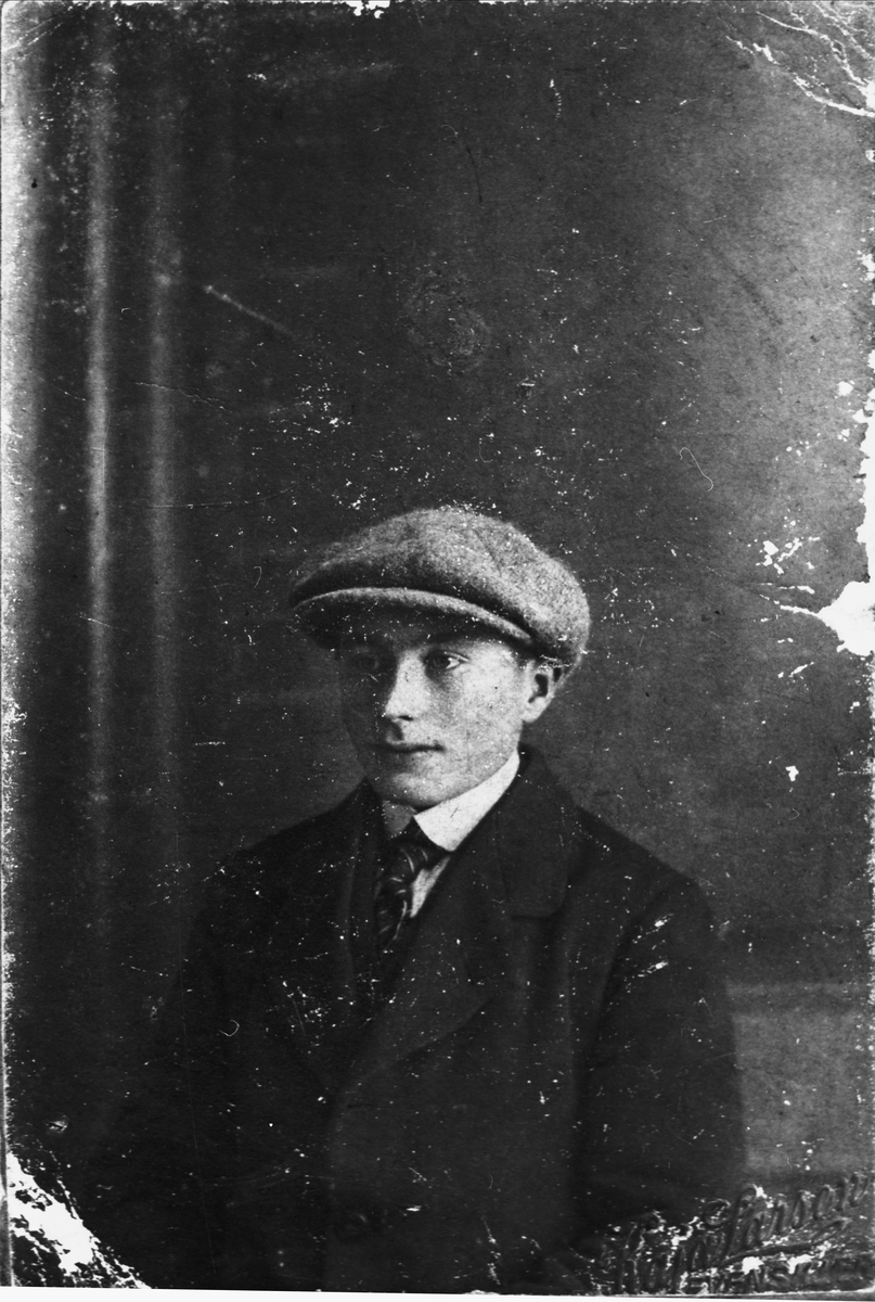 Studioportrett av ung mann kledd i dress, slips og lue. SørTroms