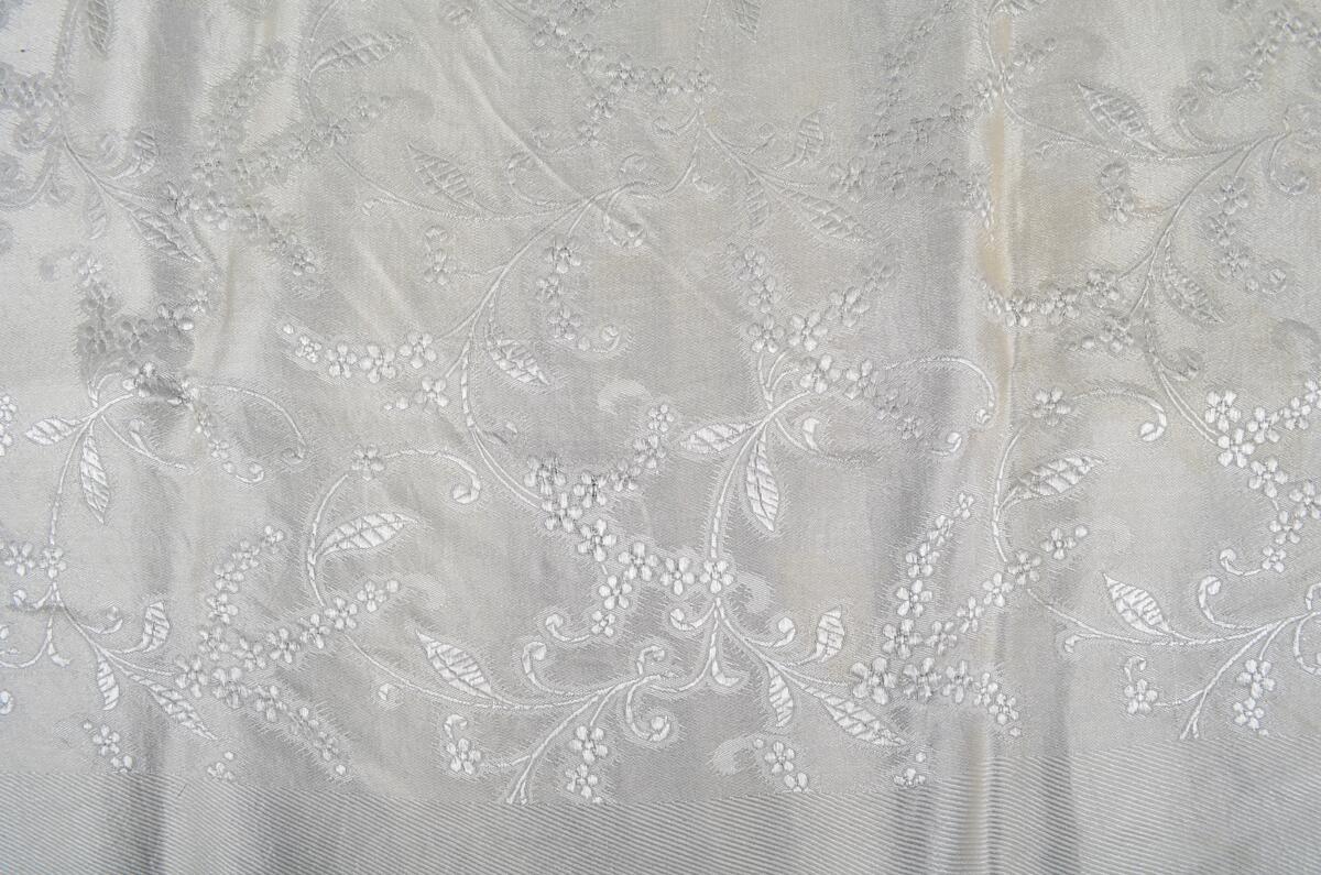 Hvitt, damaskvevd silkeskjerf med blomster- og bladmønster. Frynser på fire sider.