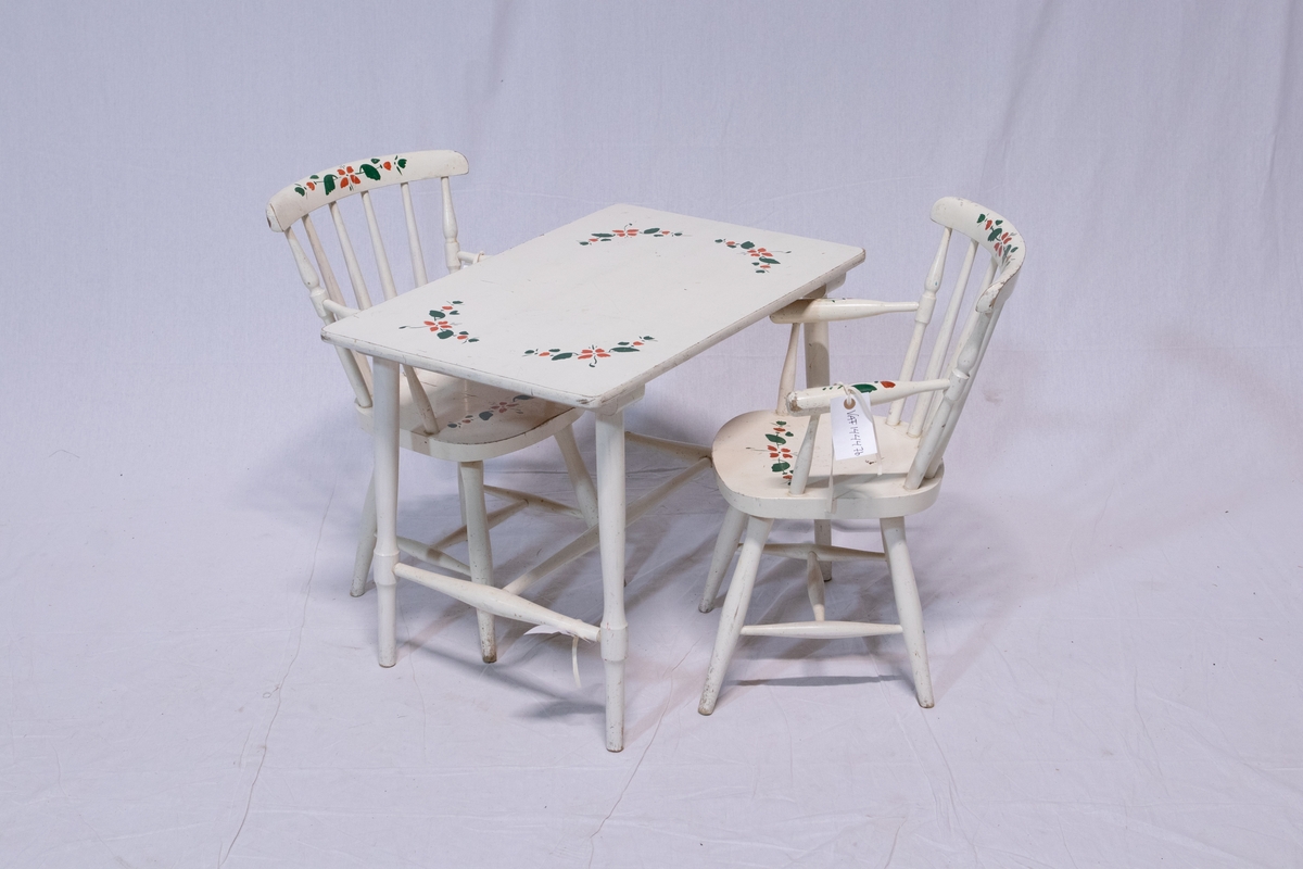 To barnestoler og bord. Hvitmalt. Enkel malt dekor i grønt og rødt på alle delene. Skal ligne blomstermotiv. Rektangulært bord med dreide ben. Stolene er pinnestoler med armlener.