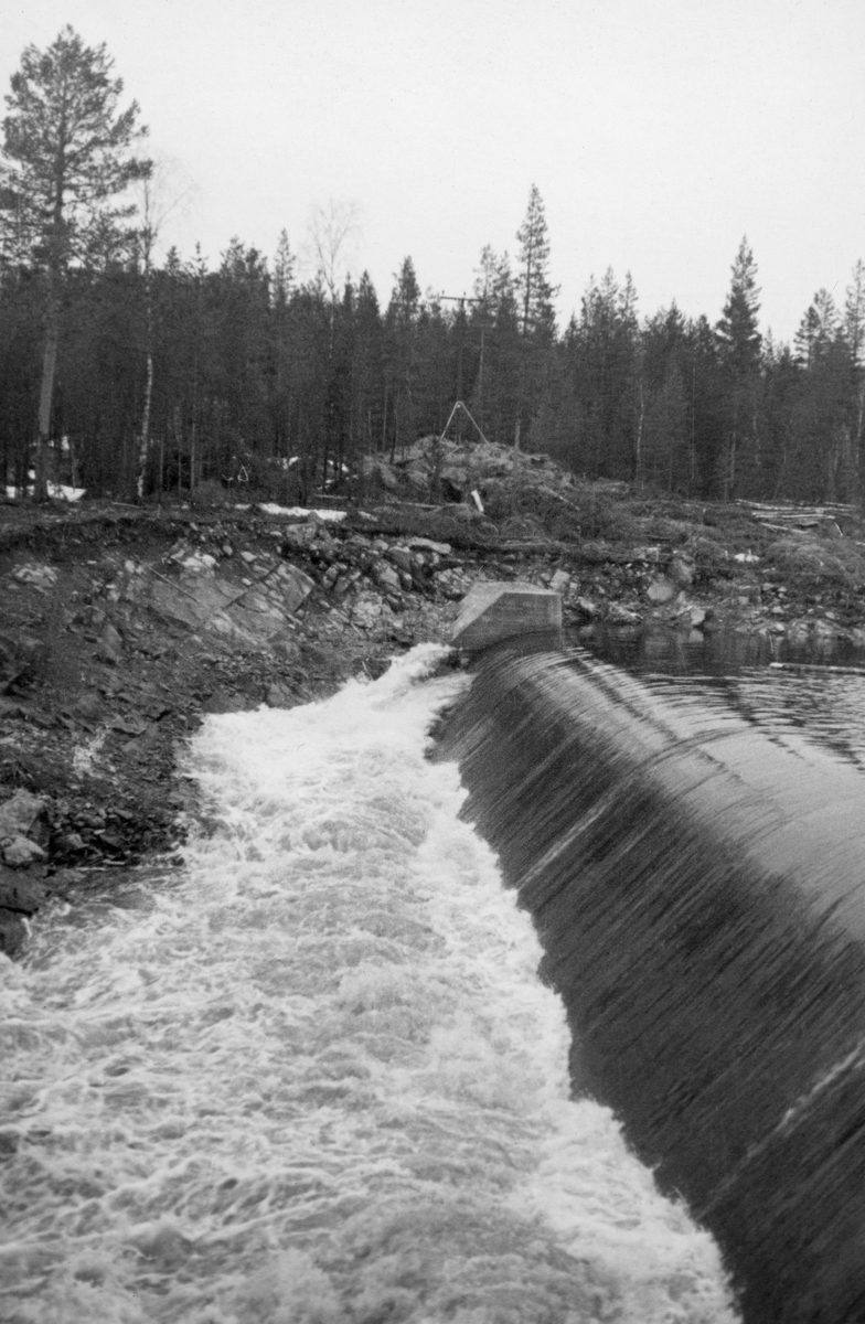 Dammen som skulle stuve opp vann til Kvernfallet kraftverk i elva Søndre Osa i Åmot kommune i Hedmark, fotografert våren 1936, like etter at anleggsarbeidet var ferdig. Her renner vannet over en avrundet terskel, utført i armert betong. Denne konstruksjonen er plassert på tvers av elveløpet, like framfor ei oppoverskrånende bergflate, som leder vannet fra nedfallssona mot den søndre elvebredden, før det føres videre vestover i det gamle elveløpet. Turbinrøret, som skulle lede vann nedover mot kraftstasjonen ved Brufallet, var også plassert på sørsida, litt til høyre for dette bildeutsnittet.

Litt mer informasjon om kraftutbygginga i Søndre Osa, og om anlegget ved Kvernfallet spesielt, finnes under fanen «Opplysninger».