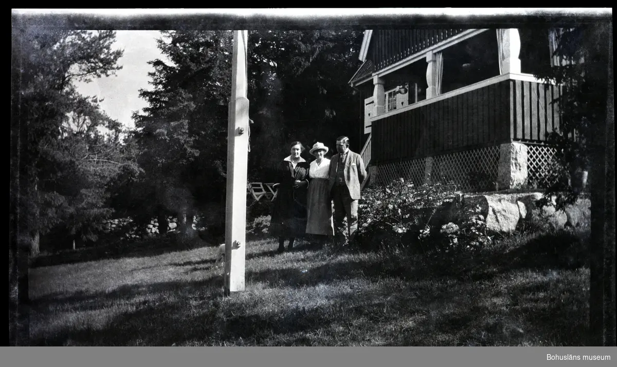 Tre personer framför en veranda i en trädgård.