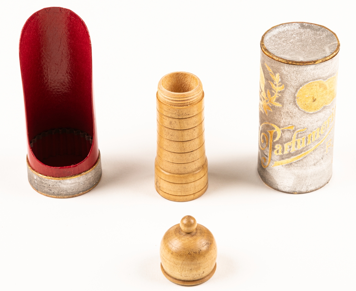 Pappersask, cylinderformad, innehållande svarvad parfymflaska i trä. Asken silverfärgad med guldfärgat tryck, invändigt röd.