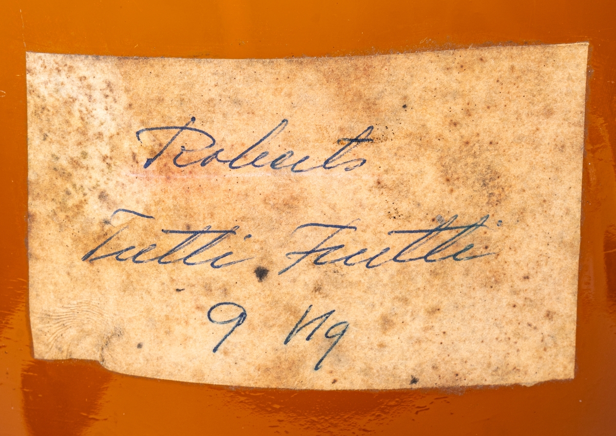 Brun glasflaska med porslinskork. Handskriven etikett: "Roberts Tutti Frutti 9KG."