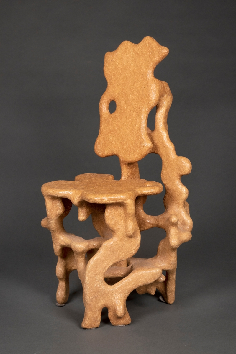 Skulpturell stol modulert i en masse laget av trestøv blandet med lim. Organisk formspråk, som om formen har vokst opp naturlig fra skogbunnen. Sitteplate, ryggplate og fem bein, alle deler med avrundede former og myke "utvekster". De negative rommene som oppstår i stolens silhuett blir en del av uttrykket.