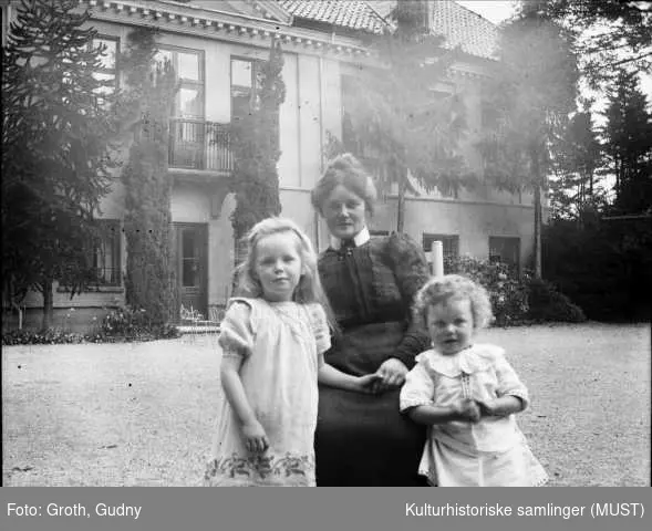Eksteriør Ledaal. Kvinne og to små jenter foran huset. Kvinnen er ant. Helene Finne, gift med maleren Gabriel Finne. Piken t.v. er antagelig datteren Assa.